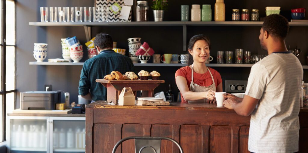 Woman working behind the counter at a cafe handing a cup of coffee to a customer.